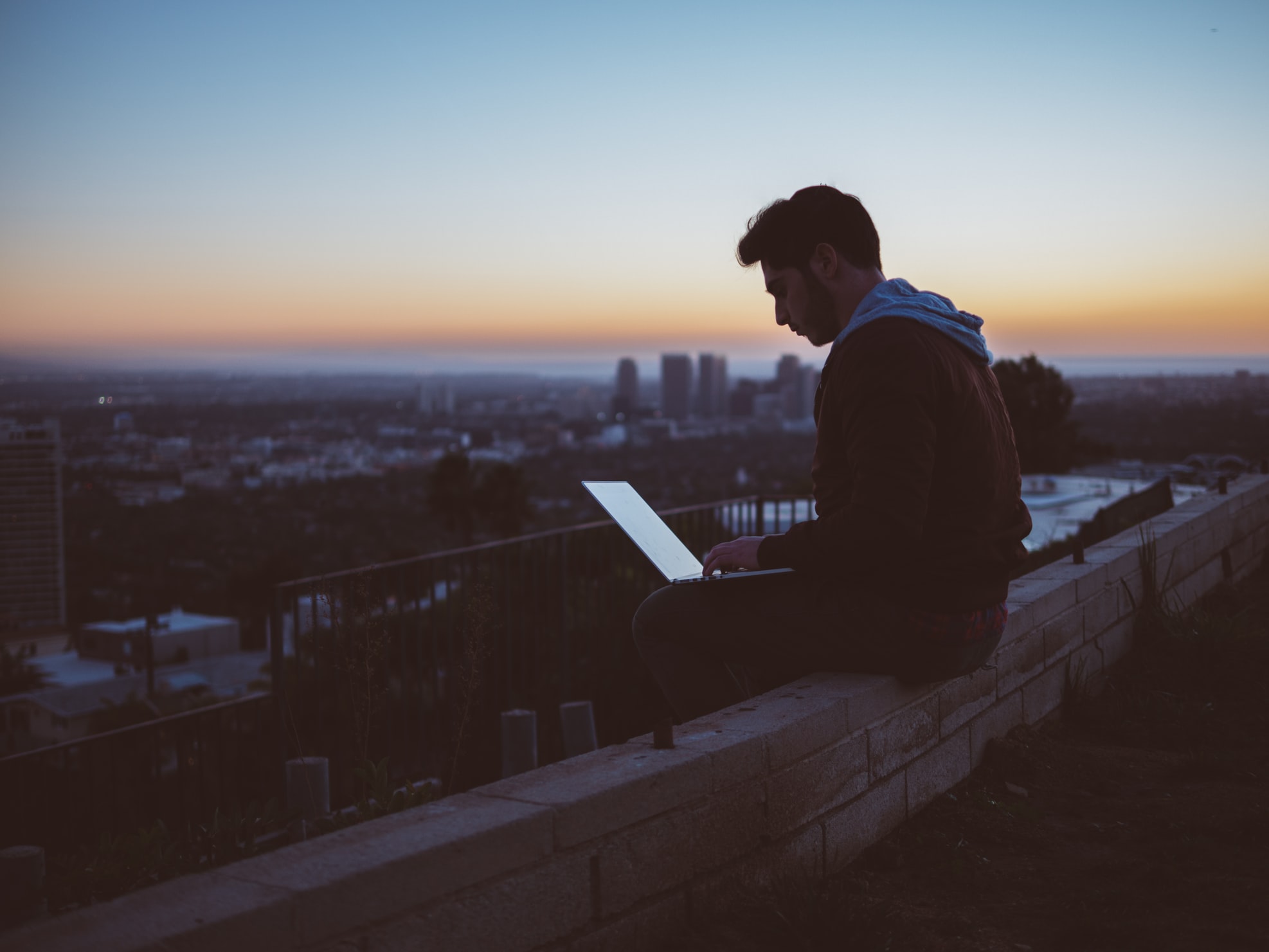 Young College Student Sitting on a Brick Wall with a Laptop