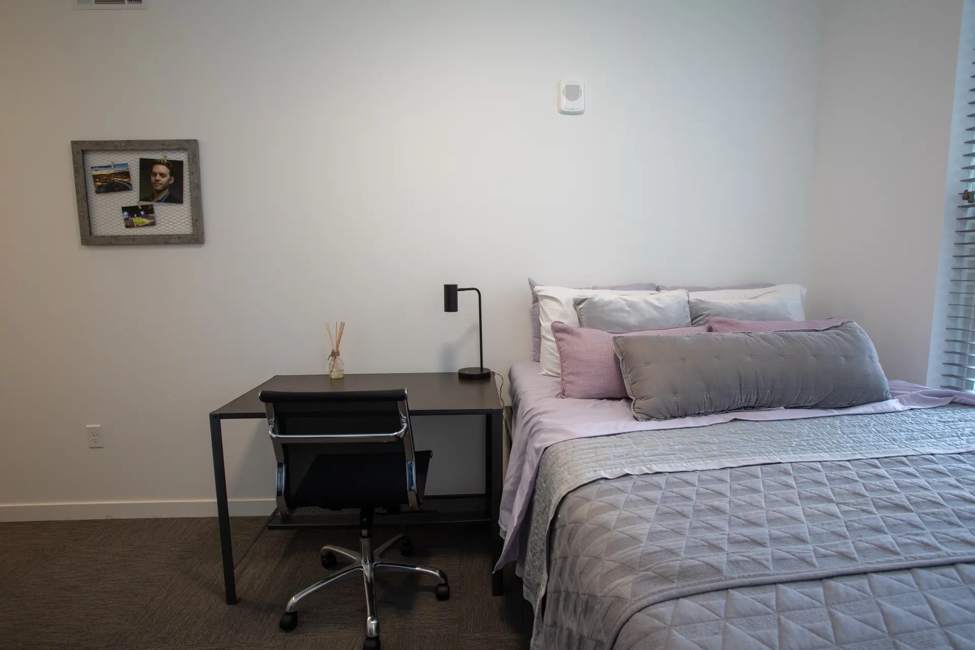 apartment bedroom large bed made with plush linens and decorative pillows. There is a desk adjacent the bed.