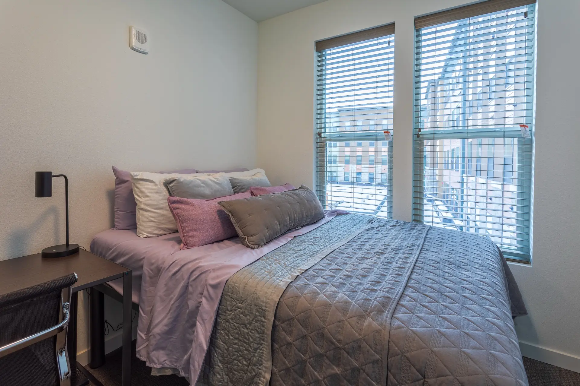 apartment bedroom large bed made with plush linens and decorative pillows. There is a desk adjacent the bed.