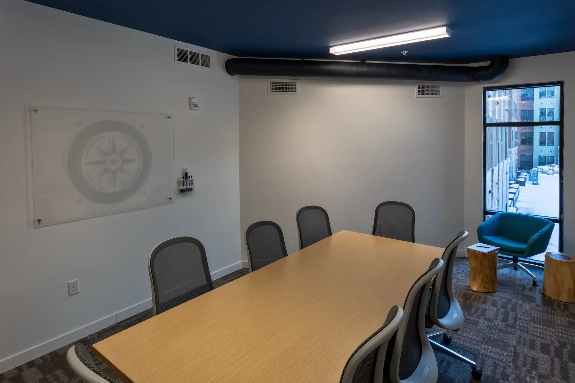 business center at roam apartments with a large conference table, mesh chairs, glass whiteboard, and a blue accent ceiling.