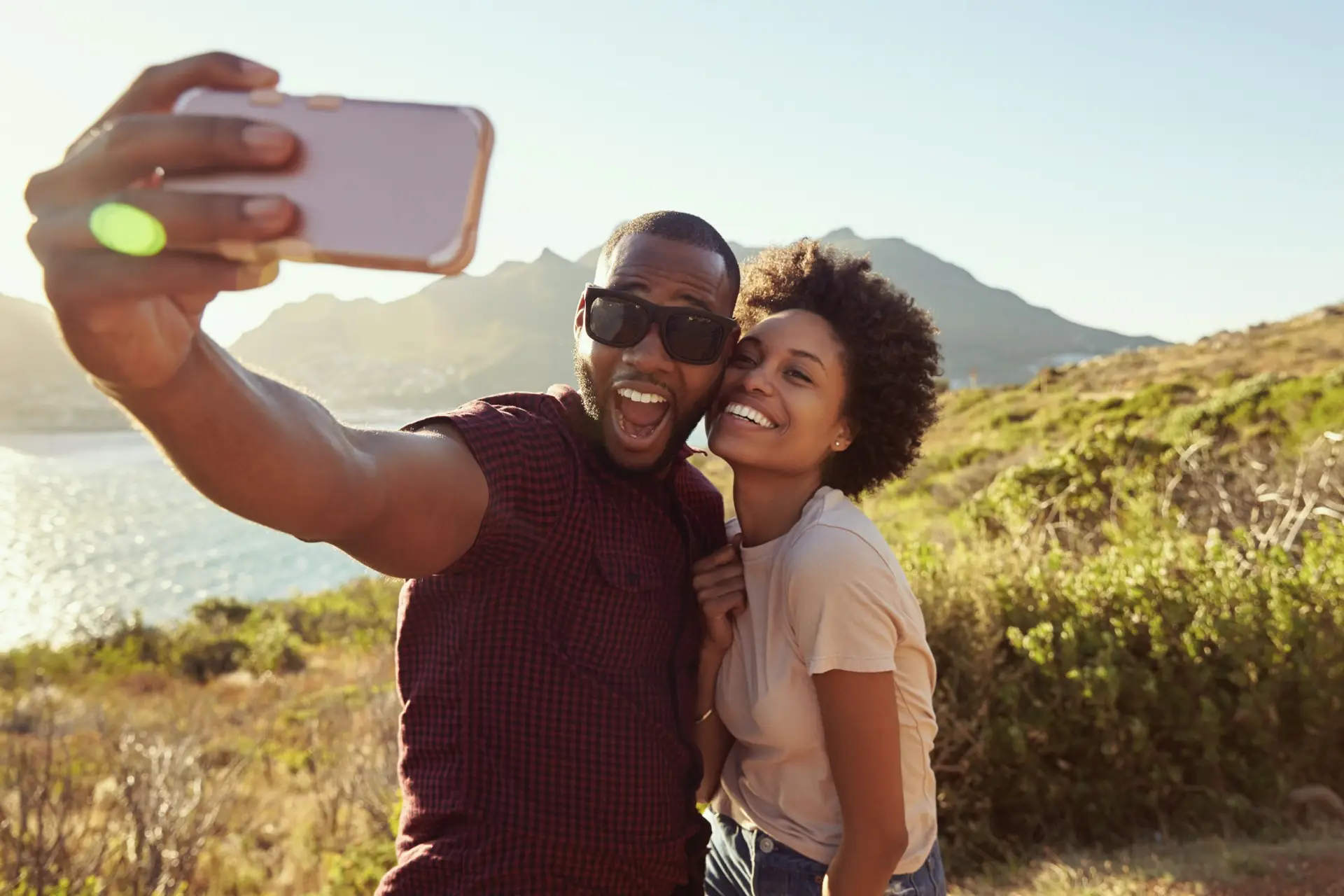A young black couple take a selfie in front of mountains in the summer